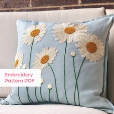 a blue pillow with white daisies on it sitting on a couch in front of a brick wall