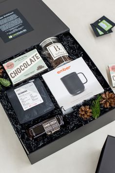 an assortment of chocolates in a black box on a white table with pine cones