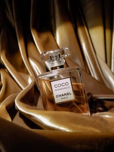 a bottle of chanel coco mademoise perfume sitting on a gold cloth covered table