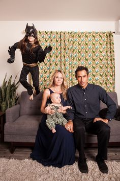 a man, woman and child are sitting on a couch in front of a batman costume