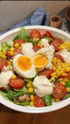 a salad with hard boiled eggs, corn and tomatoes in a white bowl on a wooden table