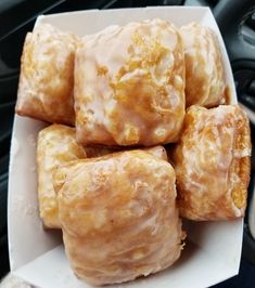 glazed donuts sitting in a white box on top of a car dash board, ready to be eaten