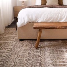 a bed with white sheets and pillows in a bedroom next to a wooden foot board