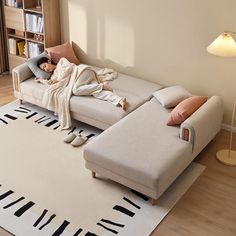 a person laying on a couch in a living room next to a book shelf and lamp