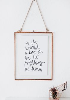 a wooden frame hanging on the wall above a white table with a plant and glasses