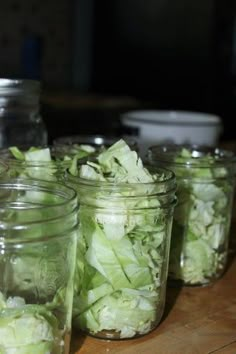 several mason jars filled with lettuce sitting on a wooden table next to bowls