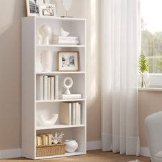 a white book shelf with books and pictures on it next to a chair in front of a window