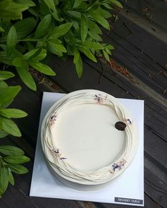 a white cake sitting on top of a wooden table next to green plants and leaves