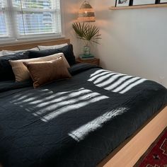 a bed with black comforter and pillows in a small room next to a window