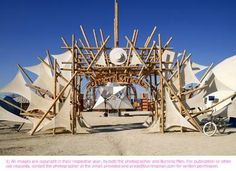 an outdoor structure made out of wooden sticks and white tents with bicycles parked in the background