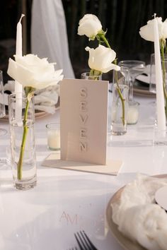 white roses are in vases on a table with place cards and candles for the centerpiece