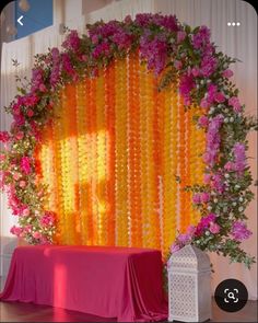 an orange and pink backdrop with flowers on the wall next to a white table cloth