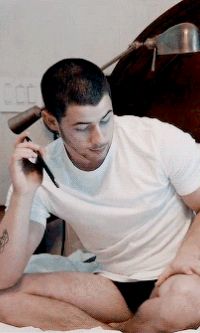 a man sitting on a bed holding a hair dryer in one hand and a comb in the other