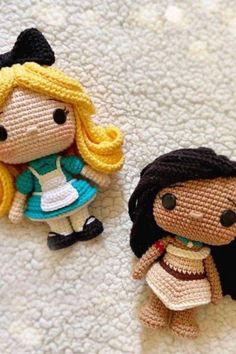 two crocheted dolls sitting next to each other on a white surface, one is wearing a blue dress and the other has yellow hair