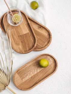 two wooden trays with drinks on them next to some palm leaves and limes