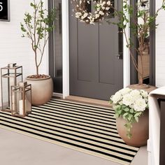 a front door with two large planters on the steps and a black and white striped rug