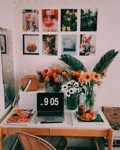 a laptop computer sitting on top of a wooden desk next to flowers and pictures hanging on the wall