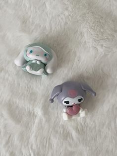 two small toy animals sitting on top of a white blanket next to eachother