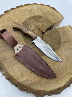 two knives sitting on top of a piece of wood next to a knife holder with a leather sheath