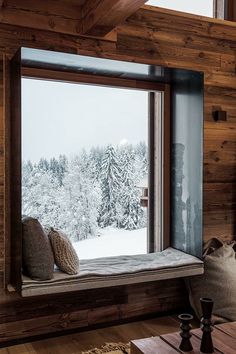 a window seat in the corner of a room with snow on the ground and trees outside