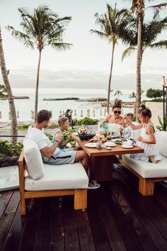 a group of people sitting around a wooden table with food and drinks on top of it