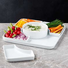 an assortment of vegetables and dip in white dishes on a marble countertop next to a serving tray