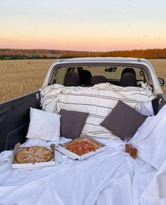 a truck bed with two pizzas and drinks on it in the middle of a field