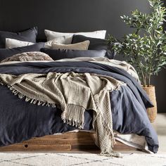 a bed with blue sheets and pillows in a room next to a potted plant