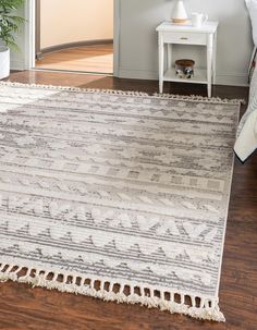 a white and gray rug with fringes on the floor in front of a bed