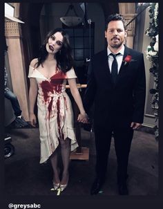 a man and woman dressed as zombies holding hands in a room with flowers on the floor