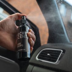 a person holding a spray bottle in their hand while sitting in the driver's seat of a car