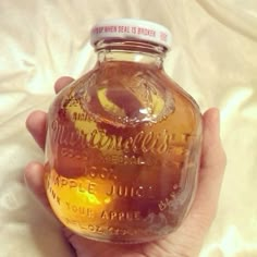 a hand holding a jar of apple cider on top of a white bed sheet