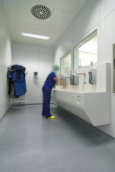 a person in scrubs is washing their hands on the bathroom sink and looking into the mirror