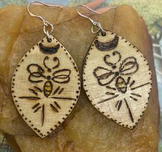 Immerse yourself in the enchanting world of nature with these unique handcrafted bee and moon earrings. These earrings showcase intricate craftsmanship, blending the art of pyrography with delicate painting. Each earring features a beautifully detailed bee design, meticulously burned into the wood and highlighted with vibrant touches of yellow paint, capturing the essence of nature's beauty.  The backs of the earrings have leather applied for extra detail.  They come with silver hooks. The earrings are shaped like leaves, topped with a crescent moon, adding a whimsical and nature-inspired touch. Perfect for nature lovers and those who appreciate the charm of handcrafted jewelry, these earrings are lightweight and comfortable to wear, making them an ideal accessory for any occasion. 🌿✨ Yellow Paint, Bee Design, Yellow Painting, Hand Painted Wood, Moon Earrings, Pyrography, Painted Wood, Handcrafted Jewelry, Jewelry Earrings Dangle