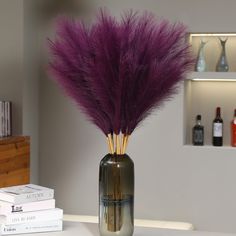 a vase with some purple feathers in it on a table next to books and bottles