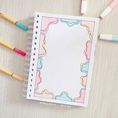 an open notebook sitting on top of a wooden table next to markers and pencils