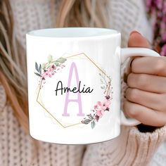 a woman holding a white coffee mug with pink flowers and the word amelie on it