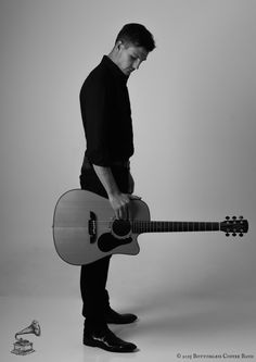 a man holding an acoustic guitar in his right hand and looking down at the ground