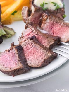 a white plate topped with steak and salad next to a fork on top of a table