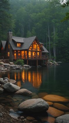 a cabin sits on the shore of a lake at night with its lights on and windows lit up