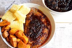 a white plate topped with meat and potatoes next to a bowl of sauce on top of a wooden table