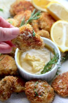 a person dipping something into a small bowl with lemon wedges on the side,