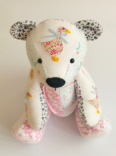 a white teddy bear with floral designs on it's face and ears, sitting against a white background