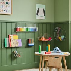 a child's playroom with green walls and wooden tables, toys on the floor