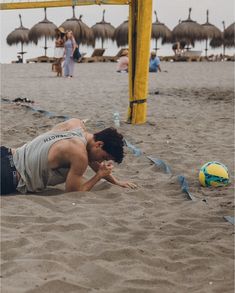 a man laying on top of a sandy beach next to a yellow pole with straw umbrellas