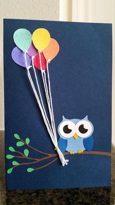 an owl with balloons is sitting on a tree branch in front of a blue card