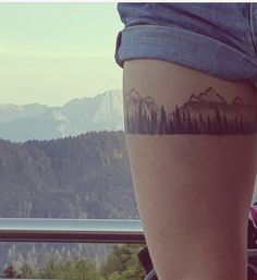 a person with a tattoo on their leg and some mountains in the distance behind them