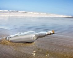 an empty bottle sitting in the sand at the beach