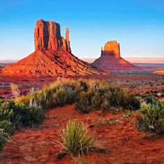 the desert is full of red sand and tall rock formations with green plants growing in front of it