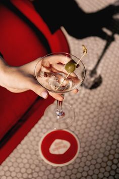 a person holding a wine glass with an olive in it and ice cream on the rim